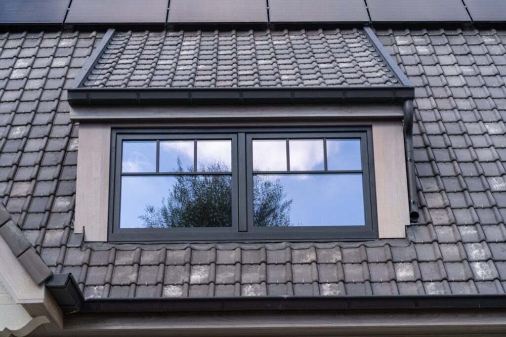 Afgewerkte dakkapel met raam in een pannendak, met zonnepanelen erboven