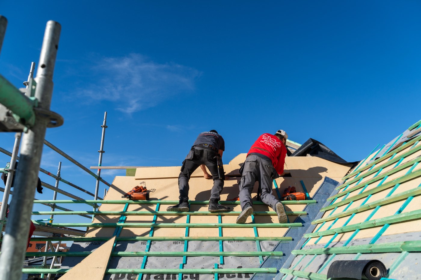 Twee dakwerkers leggen tengellatten op de onderdakplaten van een hellend dak in renovatie