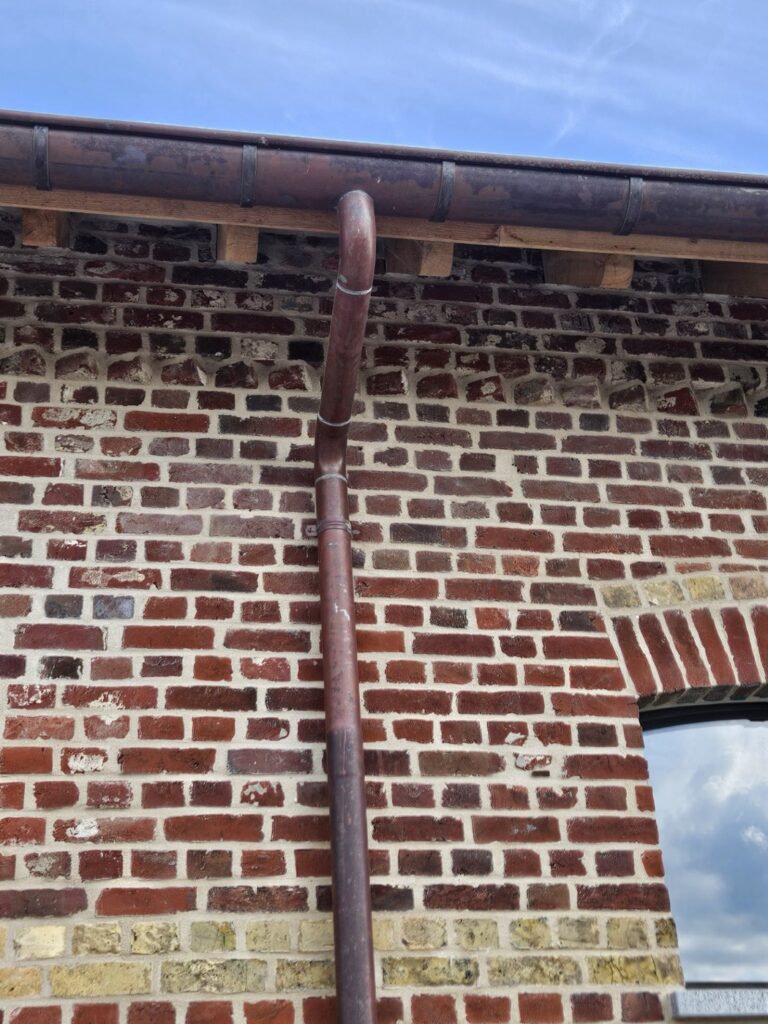 Koperen bakgoot met koperen regenafvoer tegen een gemetselde gevel