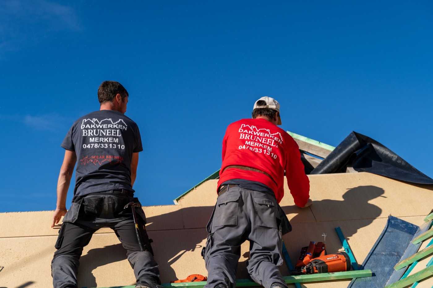 Twee dakwerkers van Dakwerken Bruneel aan het werk op een hellend dak